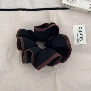 Detail of a ruffled black and brown fabric scrunchie on a neutral beige cloth.