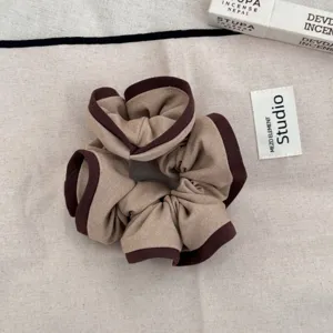 Detailed view of the fabric texture on a ruffled edge hair scrunchie in brown