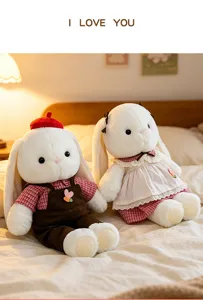 A charming pair of dressed plush Hani rabbits sitting on a warm and cozy bed scene