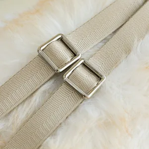 Macro detail showing the adjustable beige woven strap and metal buckle of the plush cat bag