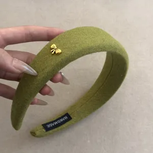 Vista de detalle de una diadema de lana verde de alta calidad con un pequeño lazo dorado.