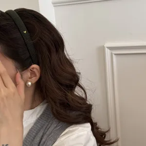 Primo piano della fascia per capelli in lana verde con cuore dorato e trama diagonale.