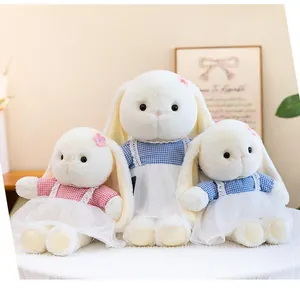 Three soft plush rabbits in pink and blue checkered dresses sitting on a white surface