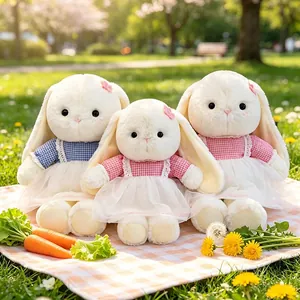 Three soft long-eared bunny plush toys in gingham dresses sitting in a sunny park.