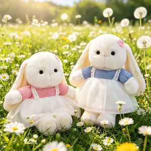 Cute plush long-eared bunny dolls in checkered dresses sitting in a daisy field