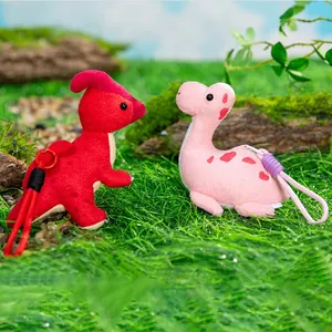 Lindos llaveros de dinosaurio de peluche con figuras rojas y rosas sobre el césped