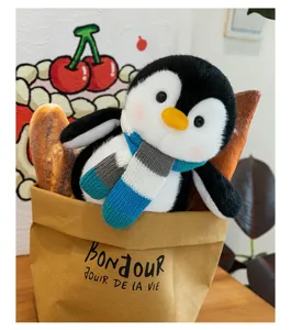 Adorable cartoon penguin plush toy wearing a striped scarf in a rustic brown paper bag