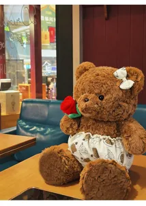 Detailaufnahme eines braunen Teddybären aus Plüsch mit einer roten Rose im Café.