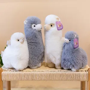 Group of four soft white and grey alpaca plush toys standing on a woven stool