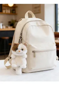 Close-up detail showing a cute fluffy cat plush pendant charm on a beige backpack