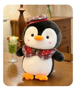 Nahaufnahme eines niedlichen Pinguin-Plüschtiers mit rotem Karohut und Fliege auf einem Tisch.