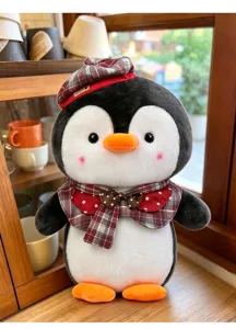 Detailansicht eines weichen Pinguin-Stofftiers mit rotem Karo-Baskenmütze und Fliege