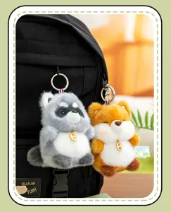 Detail view of two cute plush animal keychains, raccoon and fox, on a black backpack.