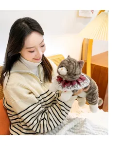 Realistic grey and white ragdoll cat plush toy with red lace collar held by a model