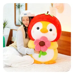 Cute penguin plush toy with strawberry hood holding flower being hugged on a bed