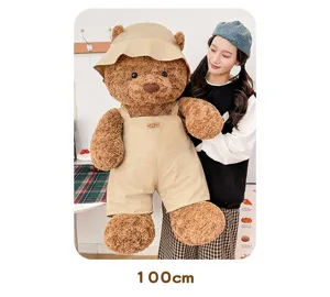 Großer Plüschteddybär mit khakifarbenem Fischerhut und Latzhose, 100 cm groß.