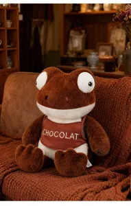 Detailed view of a cute Maillard style brown frog plush toy wearing a 'CHOCOLAT' bib on a couch