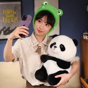 Realistische Panda-Plüschpuppe mit süßem grünem Froschhut, von einer Frau gehalten.