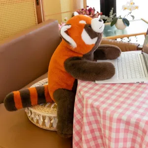 Adorable lifelike red panda plush toy sitting at a desk with a laptop for home decoration