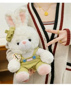 Close-up of a white plush bunny wearing green corduroy overalls held by a person.