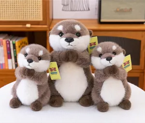 Tres adorables peluches de nutrias rezando en diferentes tamaños sobre un escritorio blanco.