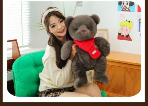 Oso de peluche gris oscuro con bufanda de punto roja, sostenido por modelo en casa.