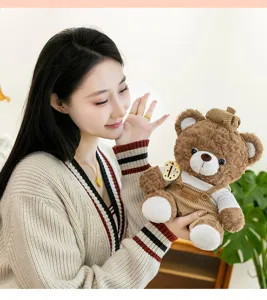 Close-up of a brown curly plush teddy bear in corduroy overalls held by an Asian woman