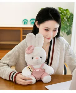 Close-up of cute white plush rabbit toy wearing pink corduroy overalls held by girl