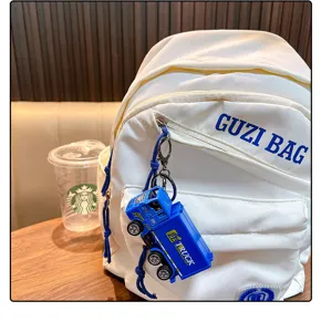 Detailed view of a blue truck toy keychain hanging on a white backpack in a cafe setting.
