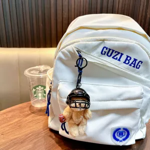 Rugby bear plush keychain hanging on a white backpack in a cafe setting