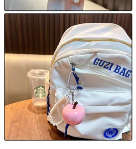 Detailopname van een roze appelhanger met parelkraalsleutelhanger aan een witte tas