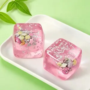 Zwei rosa durchscheinende Eiswürfel Squishy Spielzeuge mit Muscheln und Sternen.