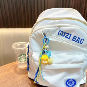 Cute yellow animal keychain with OK sign hanging on a minimalist white backpack in cafe
