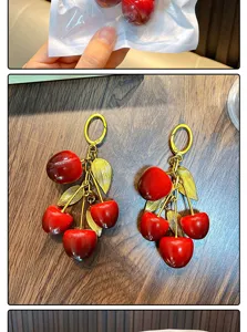 Macro view of red resin cherry fruit keychain with metallic golden leaf accessories