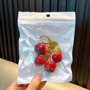 Cute red resin cherry keychain with golden leaves in a clear protective packaging bag