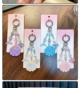 Detailed view of four glittery shell and mermaid tail acrylic charms on pink cards.