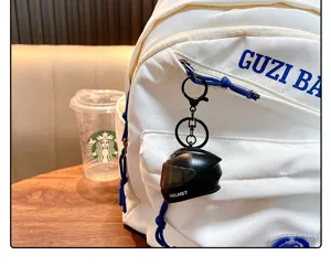 Detailed view of a black mini motorcycle helmet keychain pendant on a white backpack
