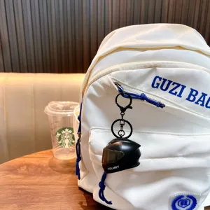 Creative black mini motorcycle helmet keychain with LED light attached to a white backpack bag