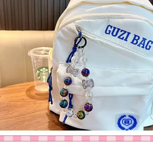 Macro detail of iridescent beaded charm with crystal bows attached to a white backpack.