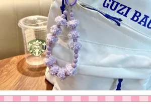Pendentif porte-clés à pompon violet et perles accroché à un sac blanc