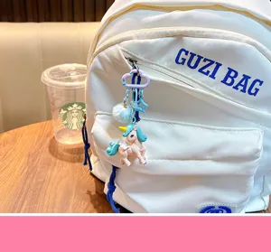 Primer plano de un lindo llavero de unicornio con pompón azul en una mochila blanca