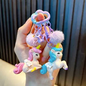 Lindo llavero de unicornio con pompones morados y caballitos en tonos pastel suaves.
