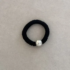 Detail view of a black elastic silk hair scrunchie with a glossy white pearl bead