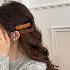Dettaglio ravvicinato di mollette BB in tessuto senape e marrone su capelli scuri ondulati