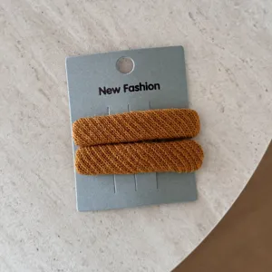 Dettaglio di due mollette per capelli in tessuto twill arancione su base grigia.