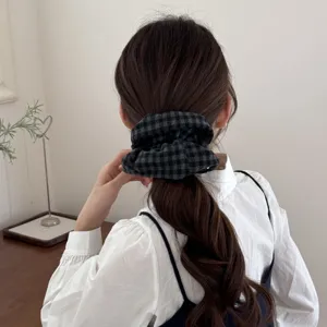 Coletero scrunchie a cuadros grises usado en una coleta de pelo castaño ondulado