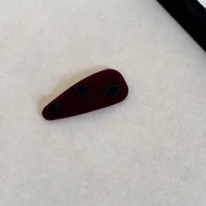 Gros plan détaillé d'une barrette en velours bordeaux ornée de petits cœurs noirs.