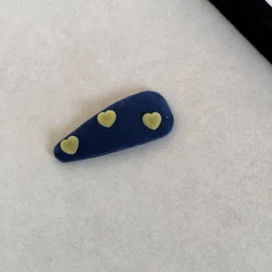 Vue détaillée d'une pince à cheveux en velours bleu marine avec trois cœurs vert tilleul