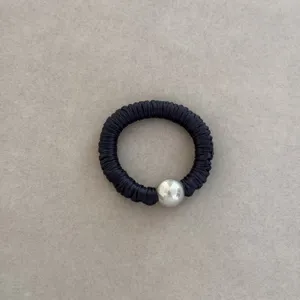 Close-up detail of a premium black silk scrunchie featuring a large silver pearl bead