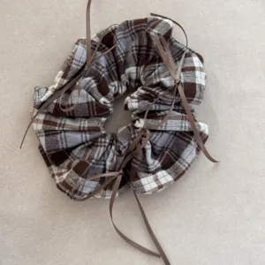 Detailed view of retro plaid scrunchie with thin brown ribbons on beige background